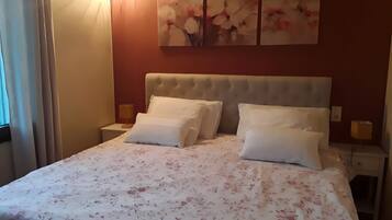 A hotel room with a large bed, two bedside tables, a wall-mounted artwork, and a window with curtains.