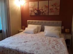 Une chambre d’hôtel avec un grand lit, deux tables de chevet, une œuvre d’art accrochée au mur et une fenêtre avec des rideaux.