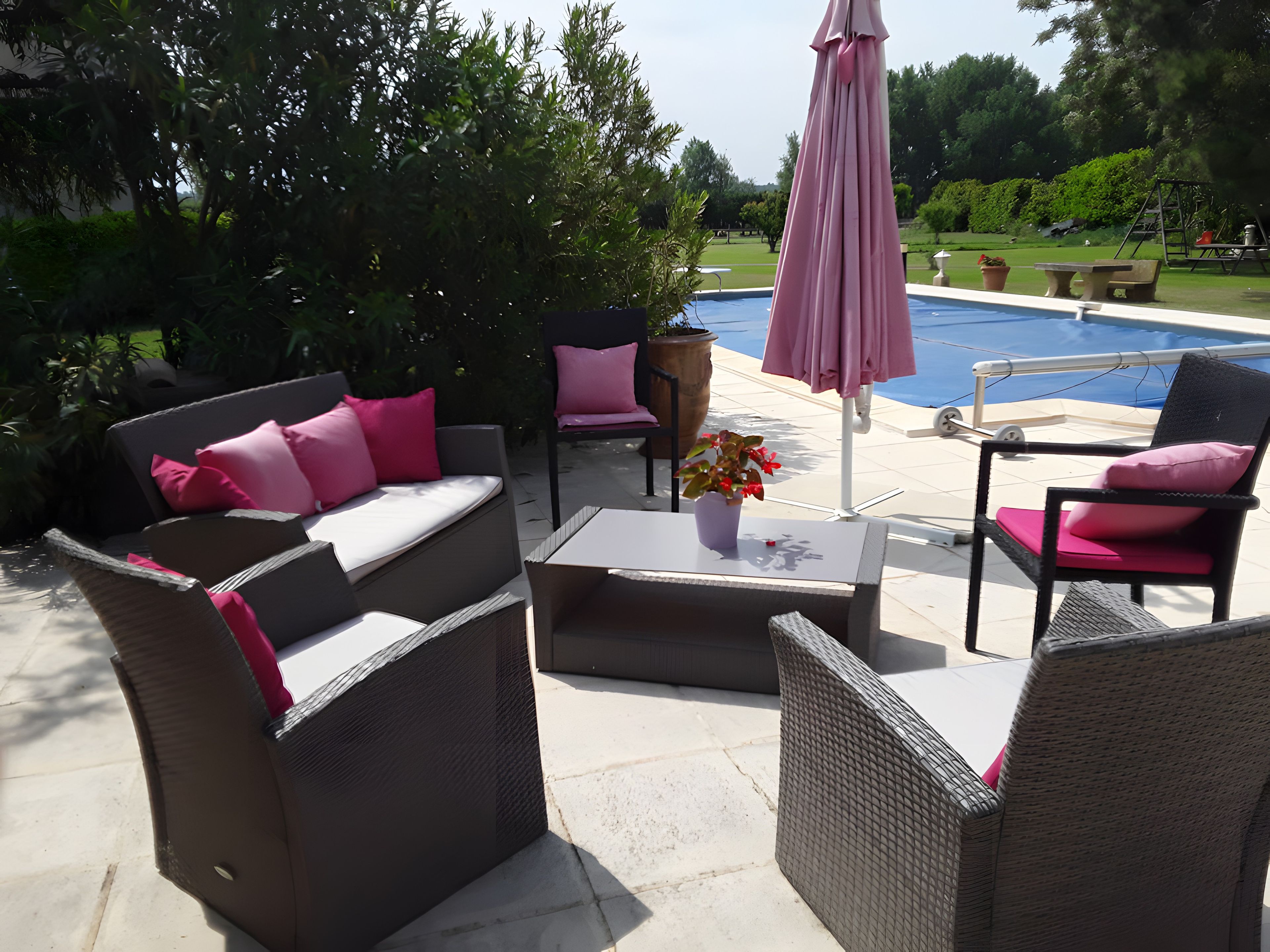 An outdoor patio with wicker furniture, a coffee table, and a pink umbrella.