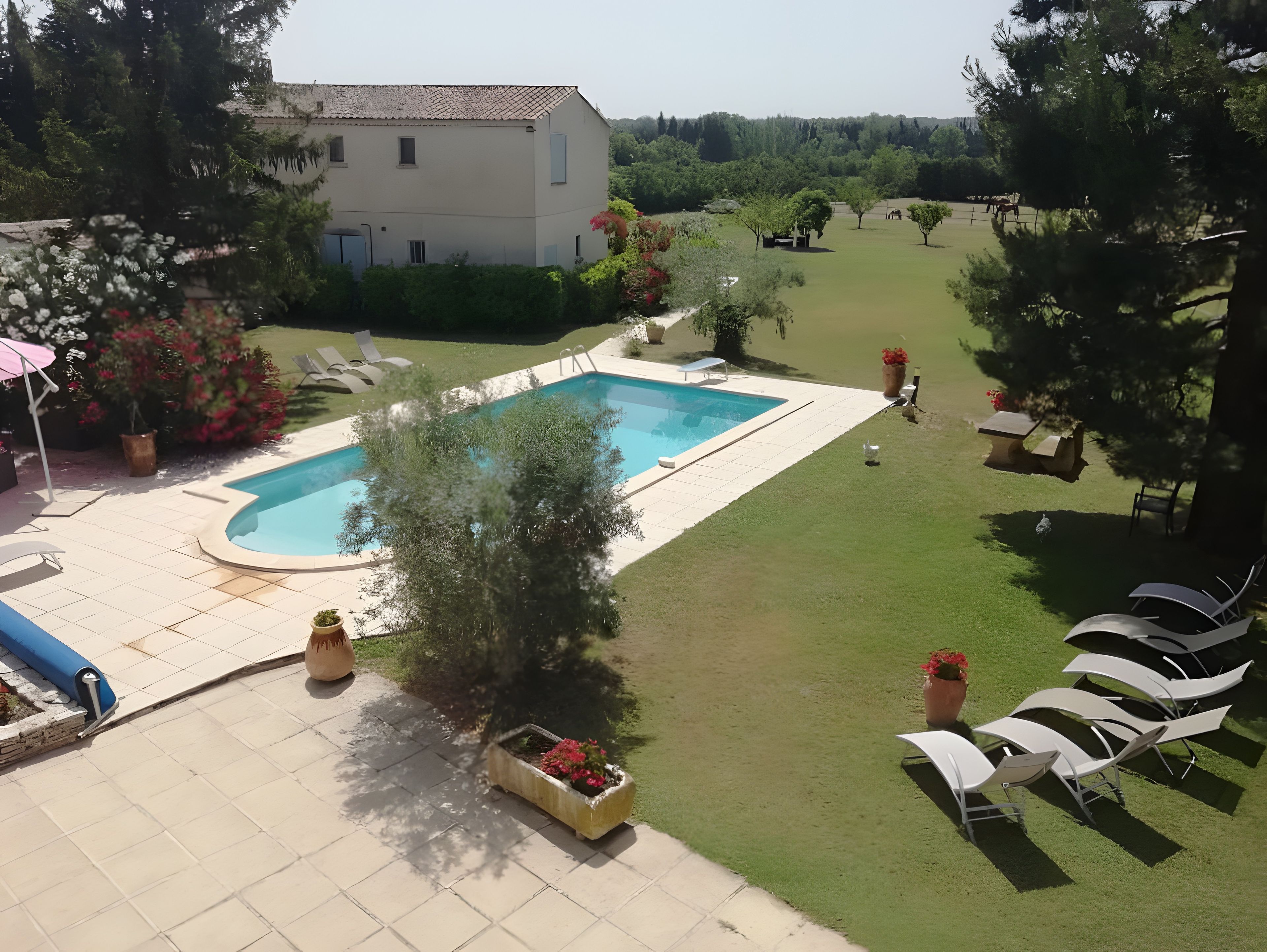 A pool area with a house in the background, surrounded by grass and trees.
