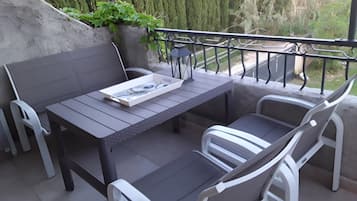 Eine Terrasse im Freien mit Tisch und Stühlen, eine Zeitschrift auf dem Tisch sowie eine grüne Bepflanzung und ein Zaun im Hintergrund.