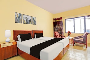 A hotel room with a double bed, a bedside table with a lamp, a chair, a small table with a vase, and a window with curtains. - Hotel O Gajuwaka Near kurmanpalem (Visakhapatnam)
