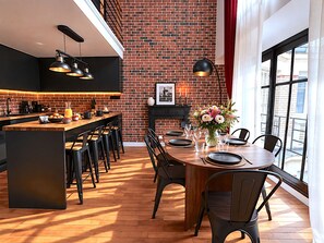 Une cuisine moderne avec un mur en briques, un plancher en bois et un coin repas avec une table dressée pour quatre personnes.