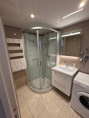 Ein modernes Badezimmer mit einer Duschkabine, einem integrierten Waschbecken und einer Waschmaschine.