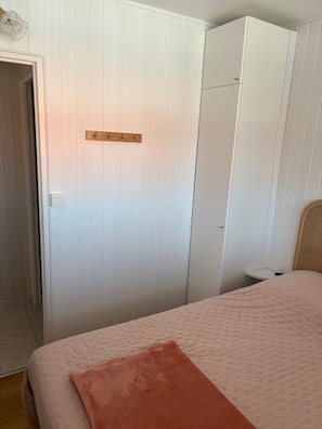 Ein Schlafzimmer mit einem Bett, einem Holz-Kleiderständer, einem Kleiderschrank und einem Nachttisch.
