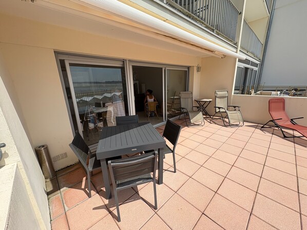 A balcony with a table and chairs, a sliding glass door, and a view of the sea. - Apartment 'Le Poséidon' with Sea View, Private Terrace and Wi-Fi (Le Crotoy)