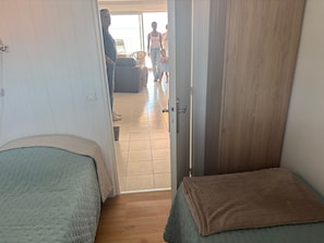 A room with two beds, a wardrobe, and a door leading to a balcony. - Apartment 'Le Poséidon' with Sea View, Private Terrace and Wi-Fi (Le Crotoy)