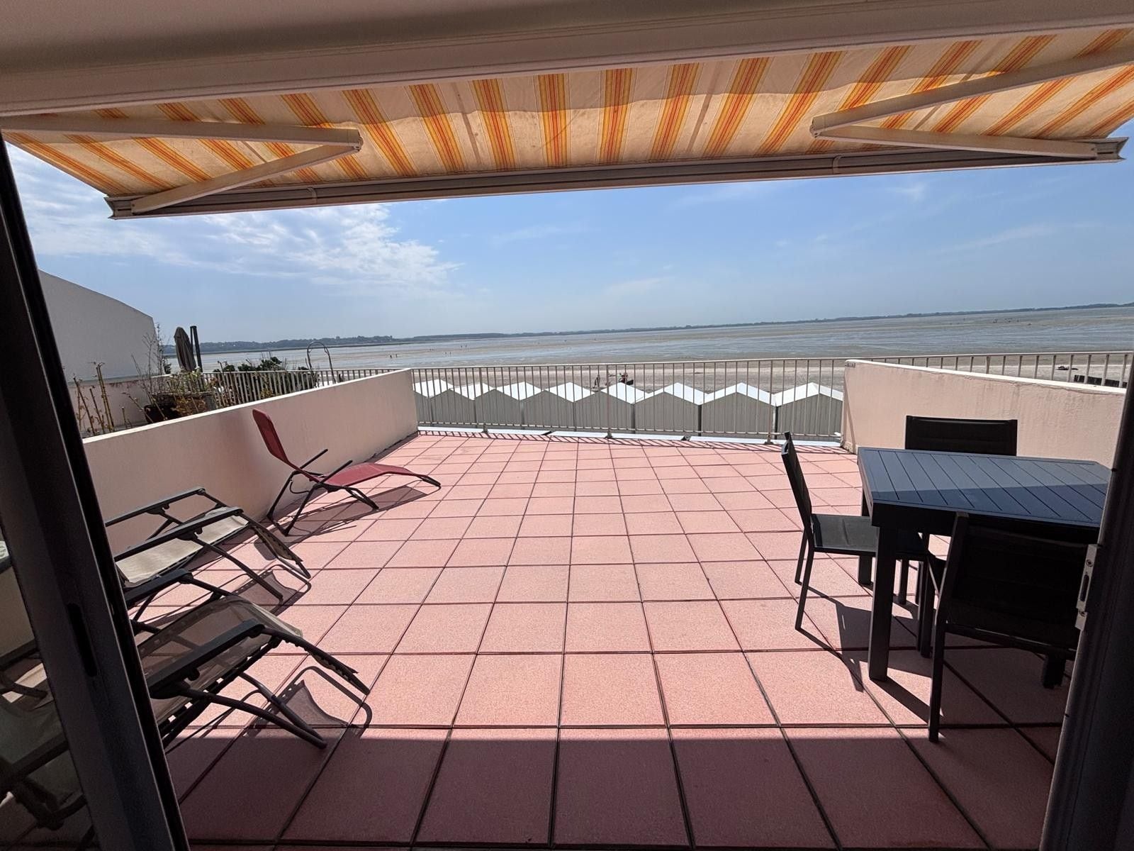 A terrace with a view of the sea, featuring a table and chairs, a covered area, and a railing.