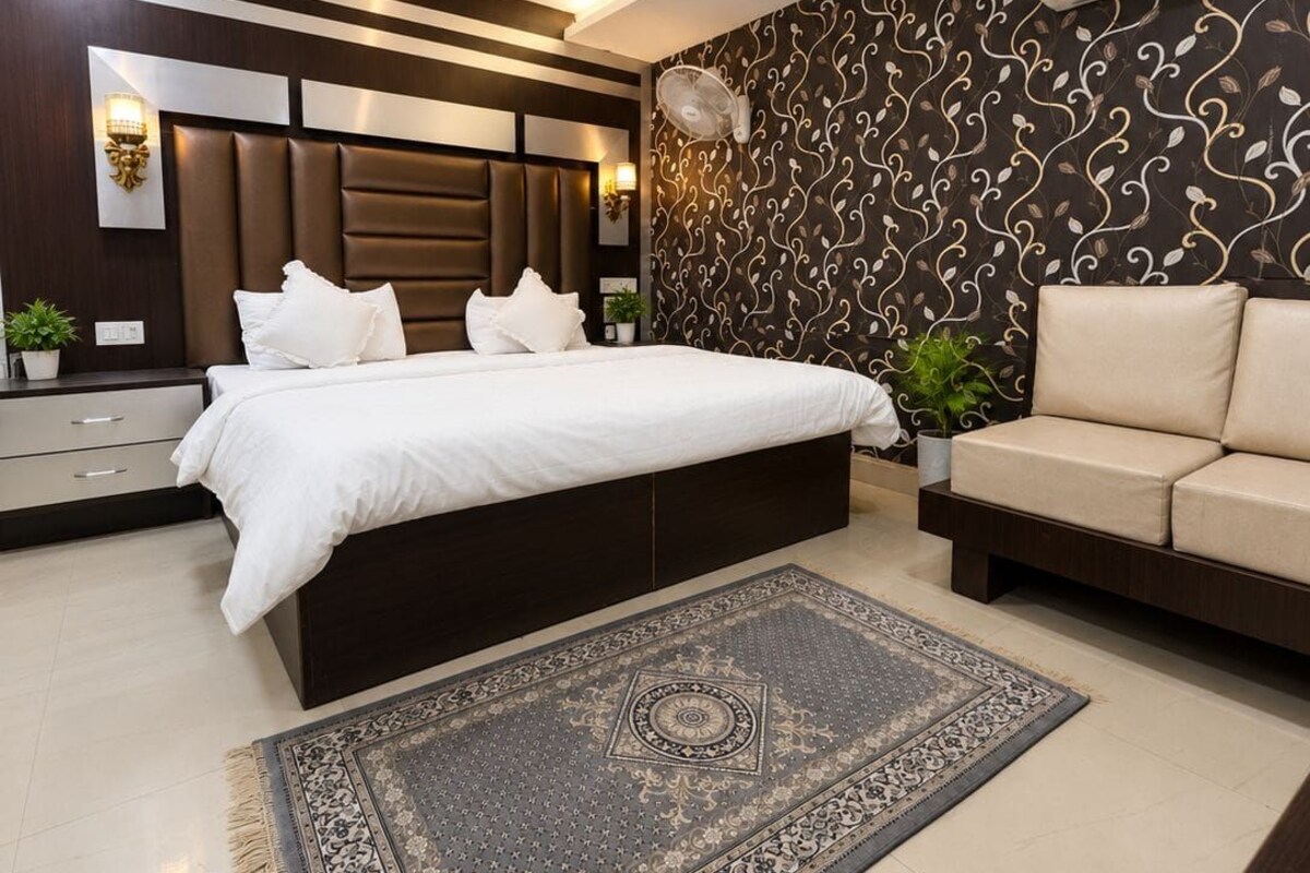 Un dormitorio moderno con una cama grande, un sofá, una alfombra estampada y un equipo de aire acondicionado.