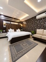 Quarto moderno com uma cama grande, um sofá, um tapete estampado e um ar condicionado.
