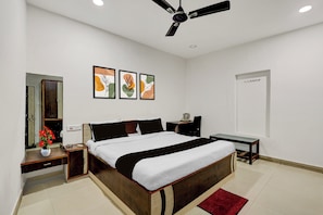 Un dormitorio con cama, mesitas de noche, un escritorio, una silla, ventilador de techo y obras de arte en la pared.