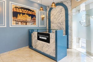 A reception desk with a sign reading 'TOWNHOUSE' and 'oro-Serviced' in a modern lobby with marble walls and a glass partition. - Townhouse Hussainpara Square (Amritsar)