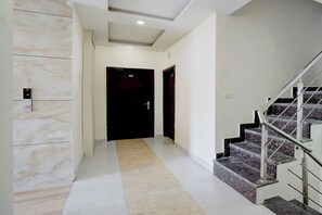 A hallway with a marble wall, a carpeted floor, a black door, and a staircase with a metal railing. - Townhouse Hussainpara Square (Amritsar)