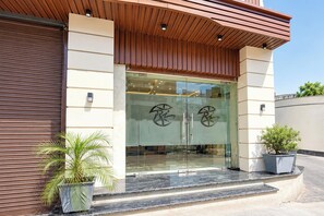 A modern building entrance with glass doors, a wooden sloped roof, and potted plants. - Townhouse Hussainpara Square (Amritsar)