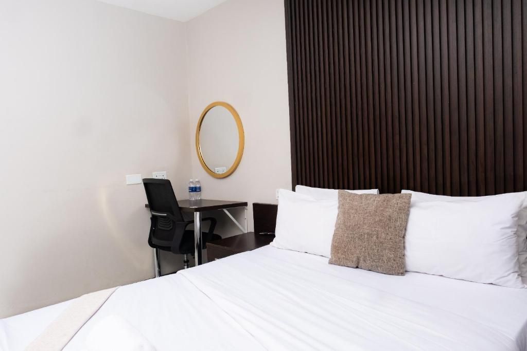 A hotel room with a bed, a desk, a chair, a mirror, and a dark-colored headboard.