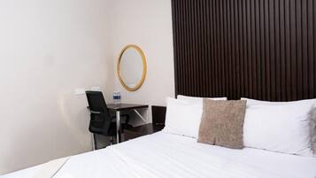 A hotel room with a bed, a desk, a chair, a mirror, and a dark-colored headboard.