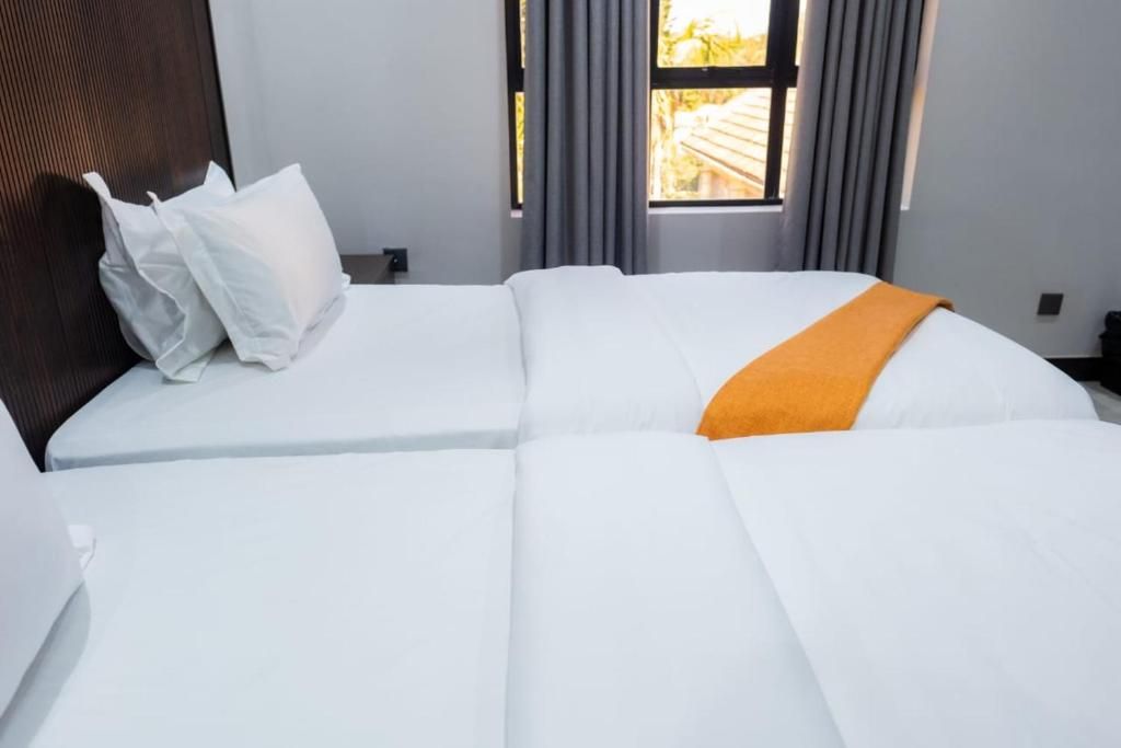 A neatly made bed with white bedding and an orange throw blanket.
