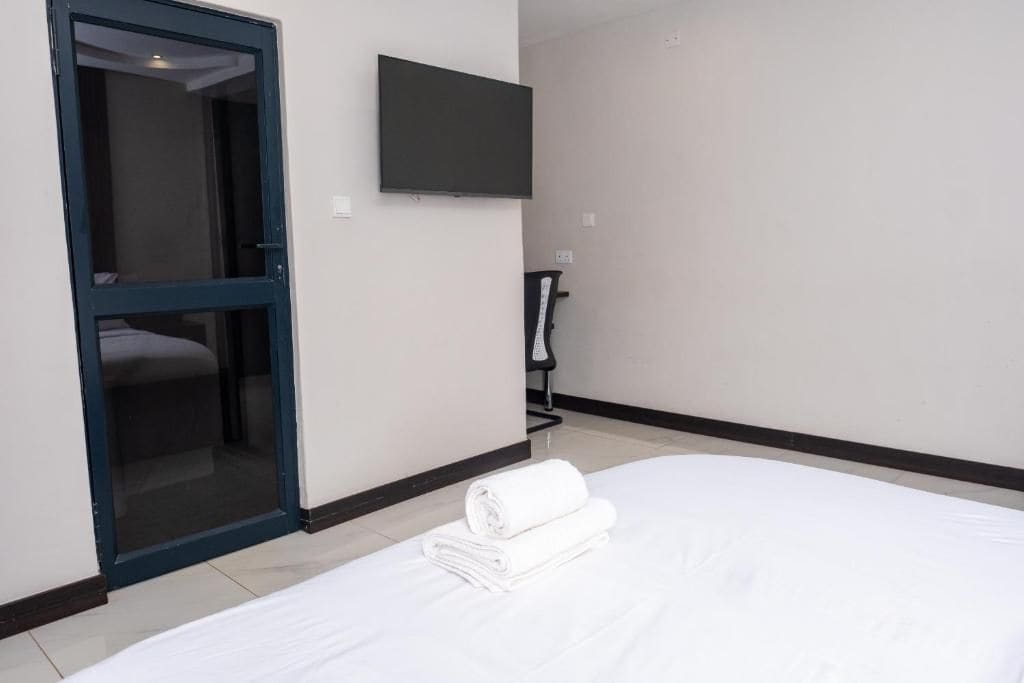 Habitación de hotel con cama, televisor montado en la pared y puerta que da a un baño.