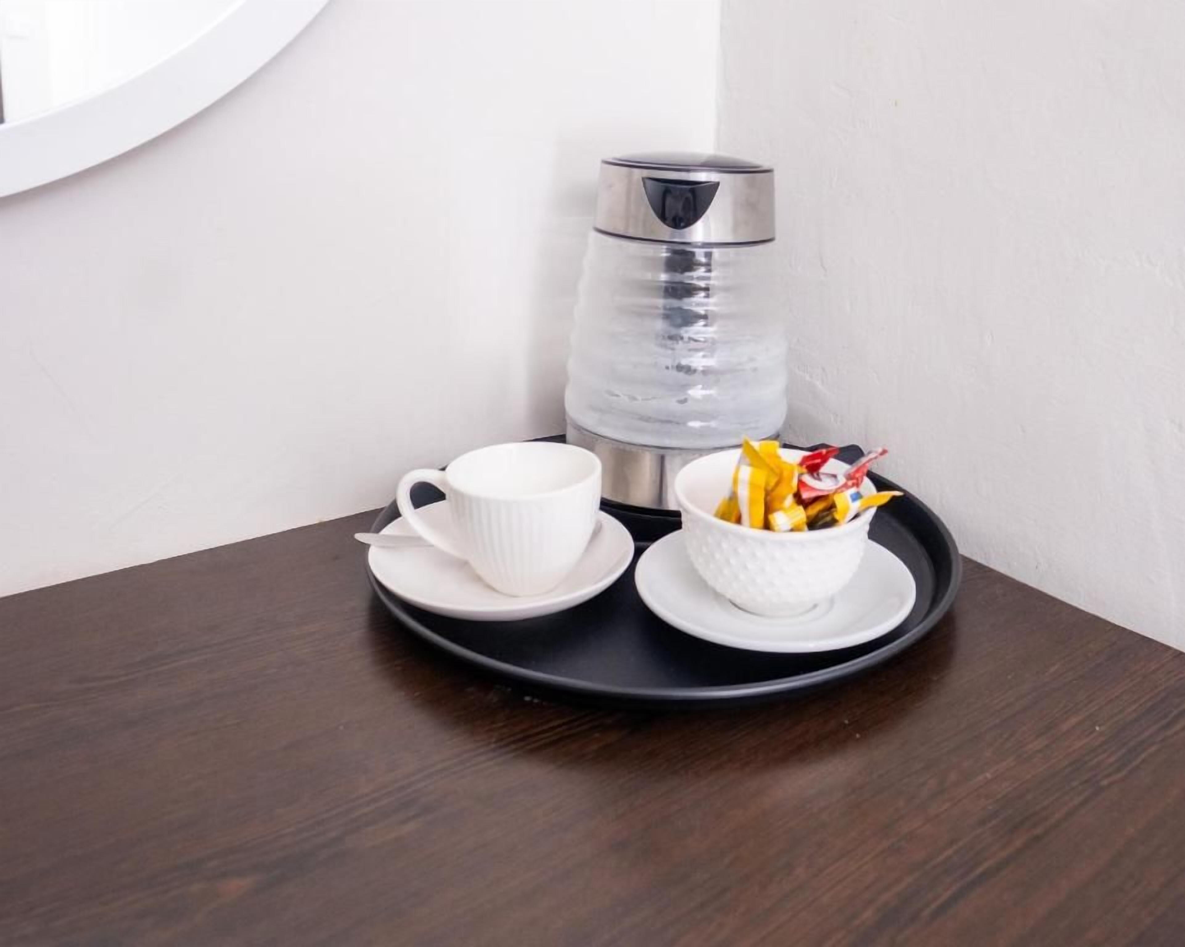 Una bandeja con una taza blanca, un platillo y un cuenco de bocadillos sobre una mesa de madera oscura.