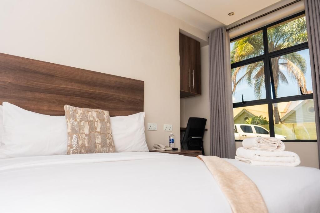 Una habitación de hotel con una cama grande, cabecero de madera, un escritorio con teléfono y una ventana con vista a palmeras.