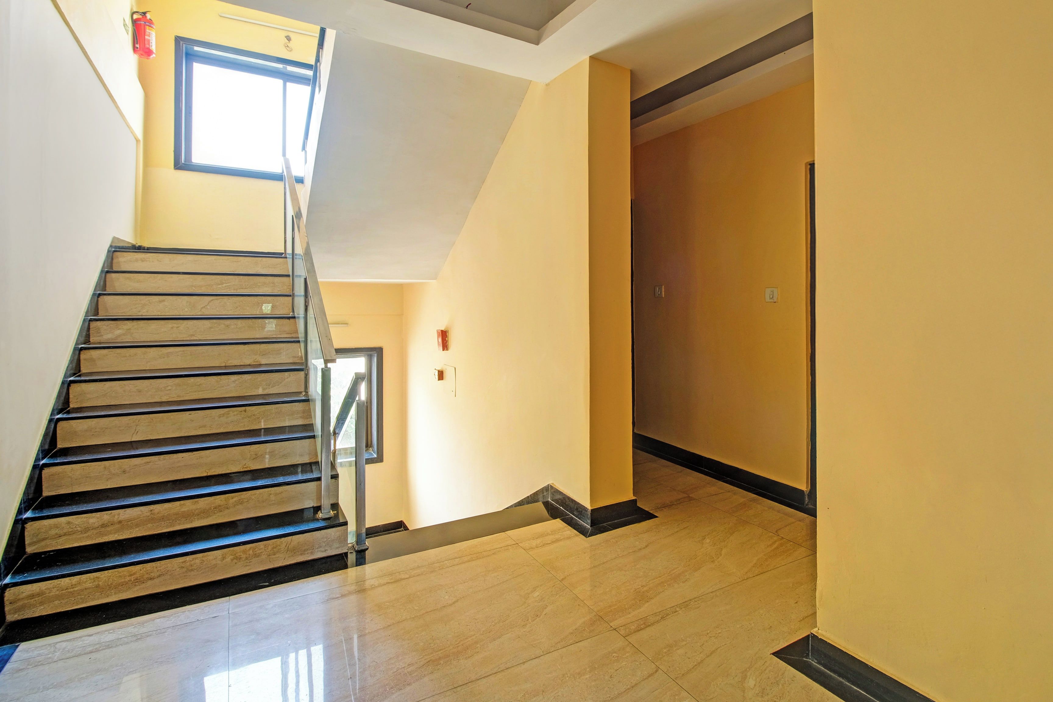 Un escalier avec une rampe menant à un palier, une porte et une fenêtre. Un extincteur est fixé au mur.