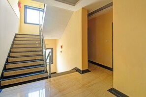 A staircase with a handrail leading to a landing, a door, and a window with a fire extinguisher on the wall. - Townhouse Oak Guwahati Airport Road (Guwahati)