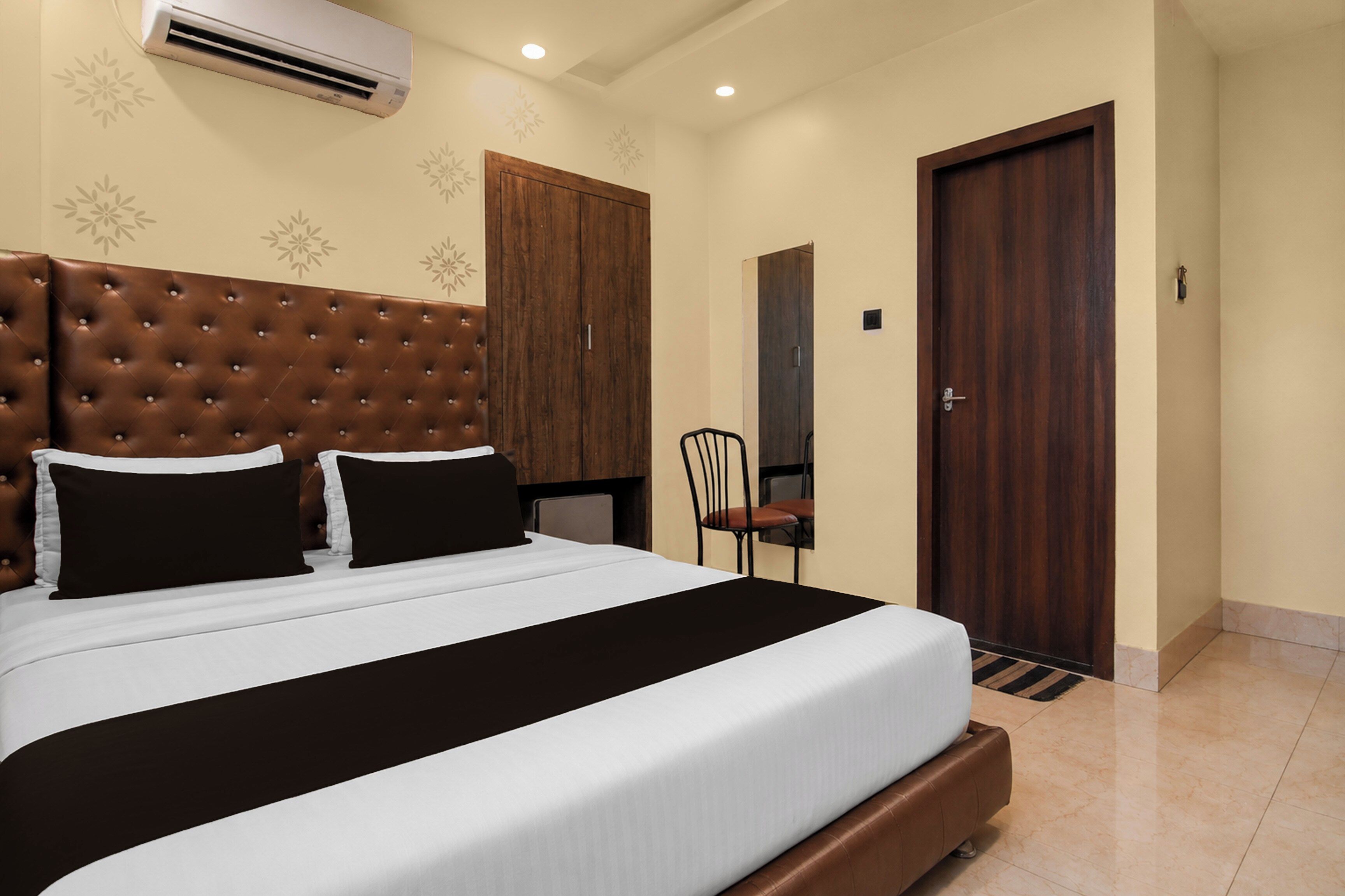 A hotel room with a large bed, a wooden wardrobe, a chair, and a door.