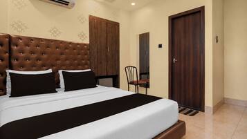 A hotel room with a large bed, a wooden wardrobe, a chair, and a door.