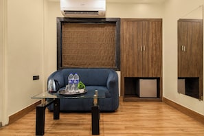 A compact room with a sofa, a small table with a kettle and bottles, and a built-in cabinet. - Collection O New Garia Railway Station (Kolkata)