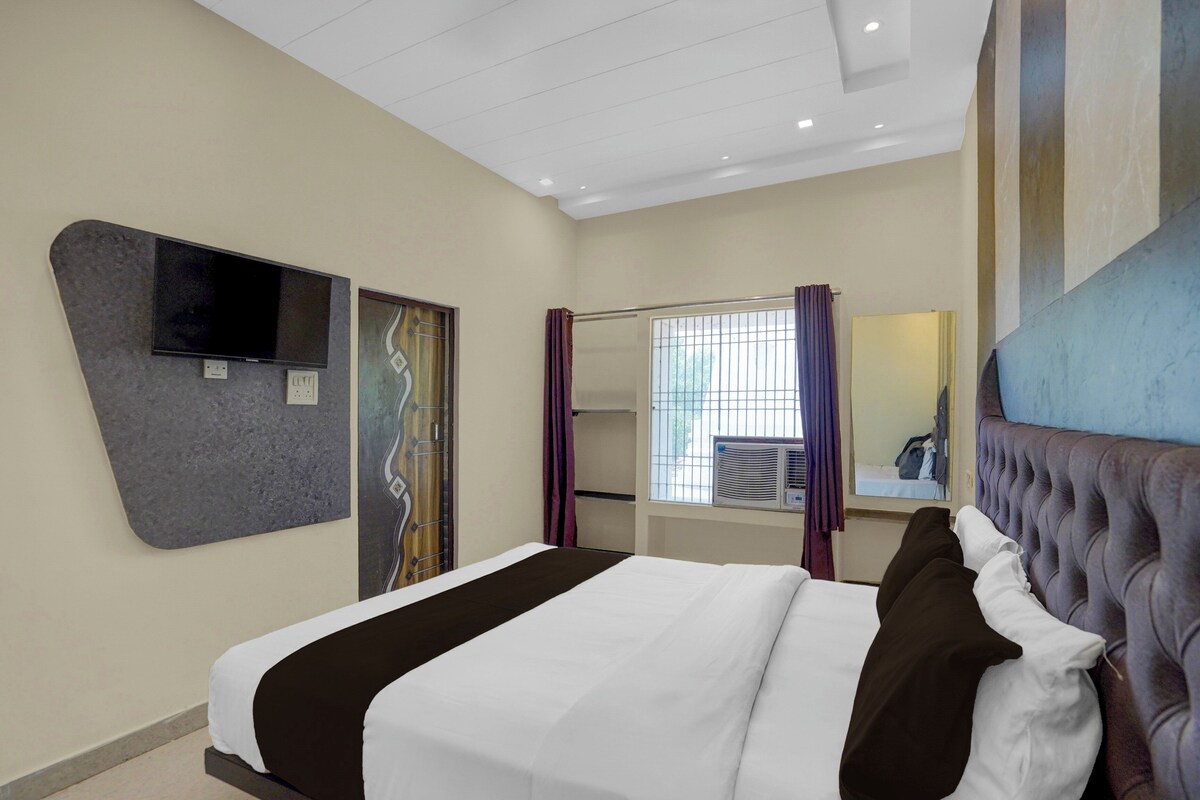Habitación de hotel con cama, televisor de pantalla plana, ventana con cortinas, equipo de aire acondicionado y espejo.