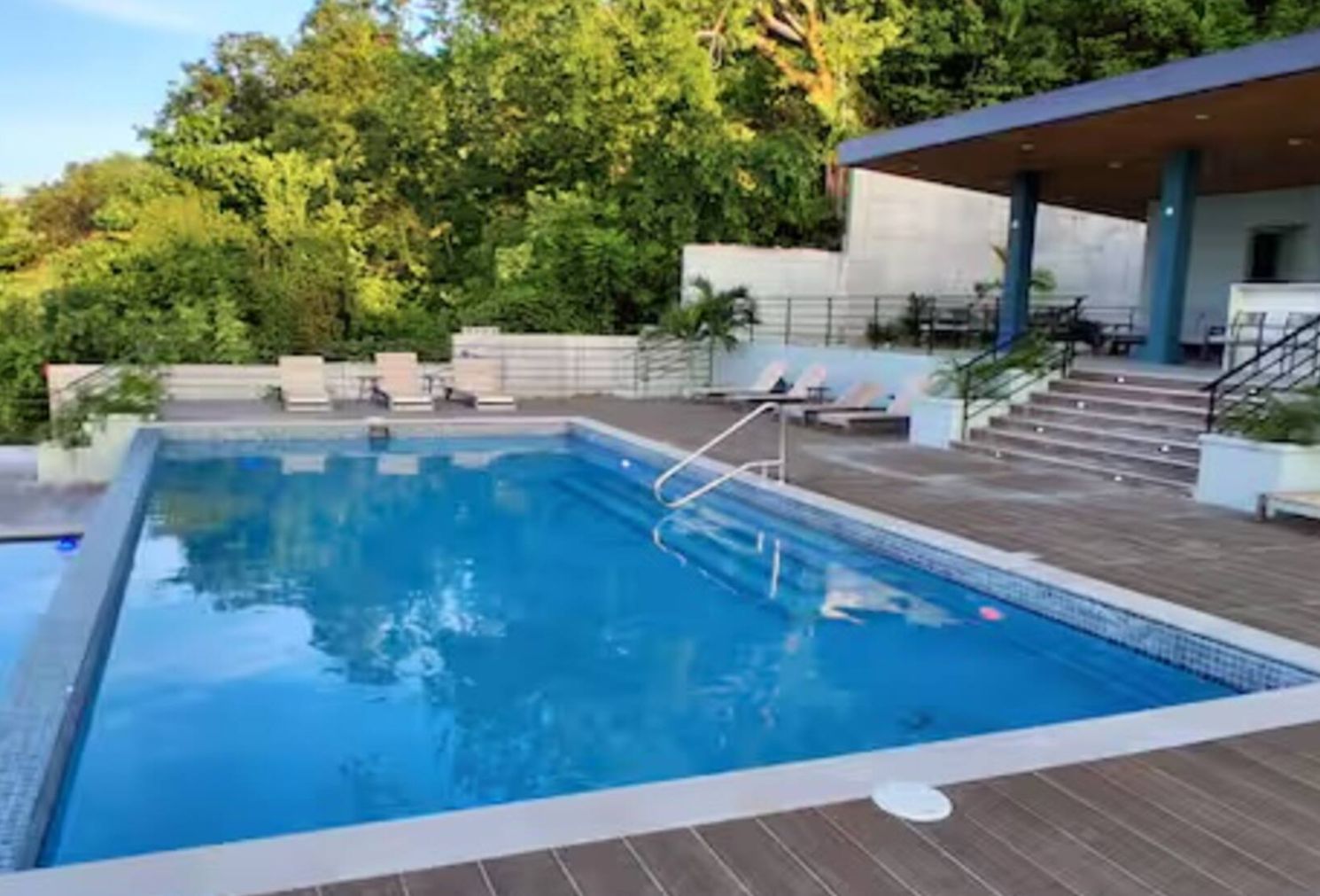 A swimming pool with a wooden deck, lounge chairs, and a covered seating area.