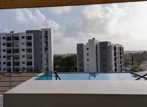 Un edifici modern amb una piscina al primer pla i altres edificis residencials al fons.