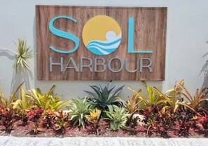 Indicador per a 'SOL HARBOUR' amb fons de fusta i un dibuix estil·litzat del sol.