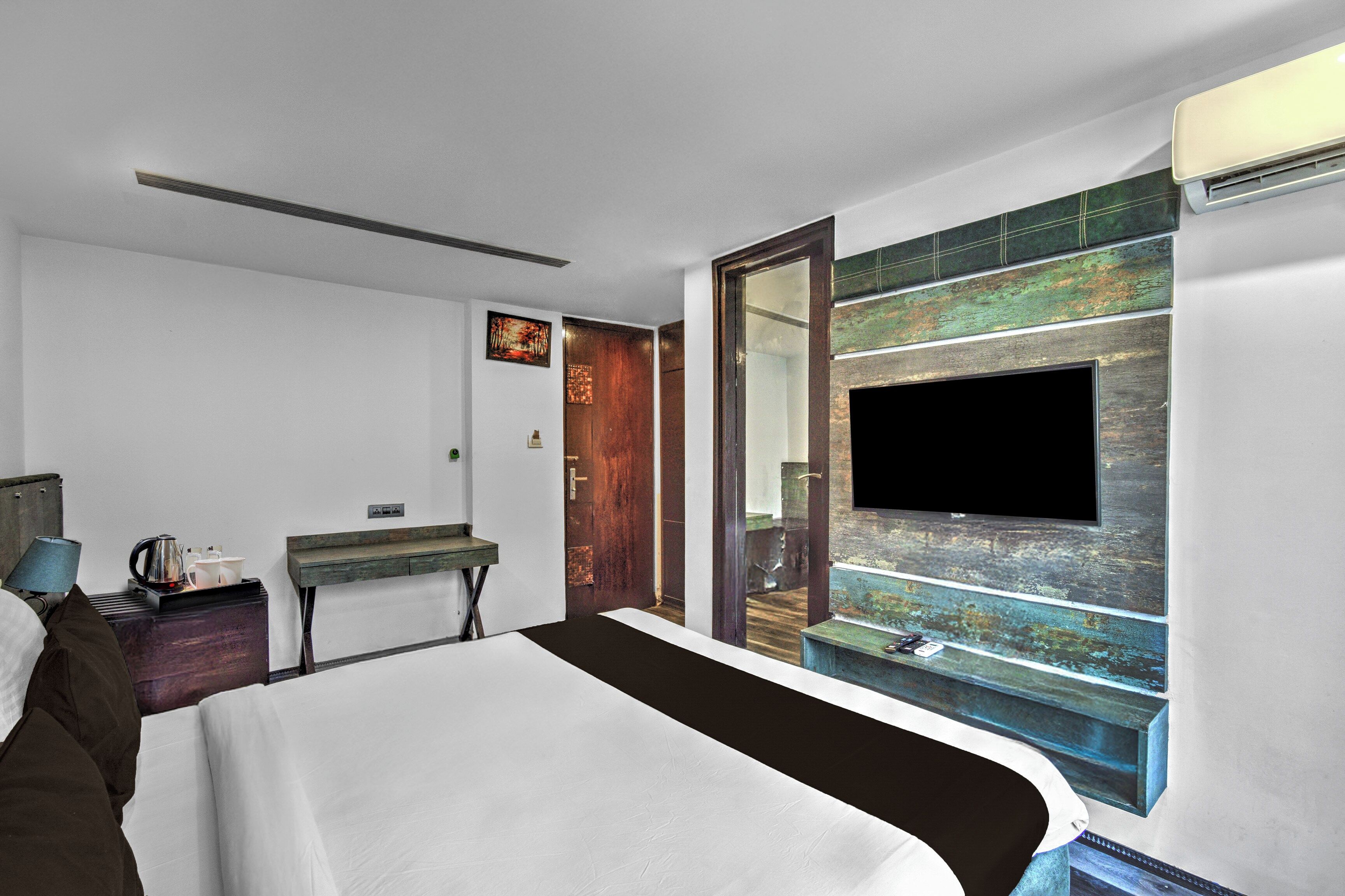A hotel room with a bed, bedside table, lamp, and a television mounted on a wall with a decorative panel.