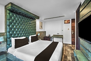 A hotel room with a large bed, a headboard, a bedside table, a nightstand, a desk, a chair, a television, and a door. - Townhouse Oak Hotel Banjara Hill (Hyderabad)