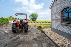 A red tractor parked on a paved driveway in front of a brick building with a large window. - Farmhouse Retreat for 20 Guests in Snelrewaard (Snelrewaard)