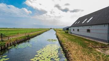 Un canale con ninfee, un edificio in mattoni con tetto spiovente e un campo verde sullo sfondo.