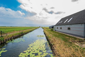 A canal with water lilies, a brick building with a sloped roof, and a green field in the background. - Farmhouse Retreat for 20 Guests in Snelrewaard (Snelrewaard)