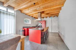 A modern kitchen with a central island, red cabinets, and a wooden ceiling. - Farmhouse Retreat for 20 Guests in Snelrewaard (Snelrewaard)