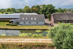 A building with a tiled roof, a pond with lily pads, and a tractor in the background. - Farmhouse Retreat for 20 Guests in Snelrewaard (Snelrewaard)