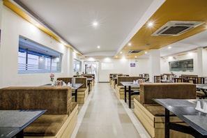 A restaurant with booths and tables, a long counter, and a view of the street through large windows. - Collection O Saraswathi Park (Visakhapatnam)