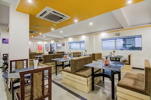 A restaurant with booths and tables, ceiling fans, and a view of the outside. - Collection O Saraswathi Park (Visakhapatnam)