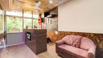 A hotel reception area with a wooden reception desk, a pink upholstered sofa, and a ceiling fan.