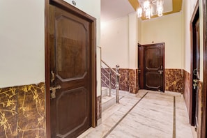 Un pasillo con dos puertas de madera, una escalera de mármol y un candelabro.