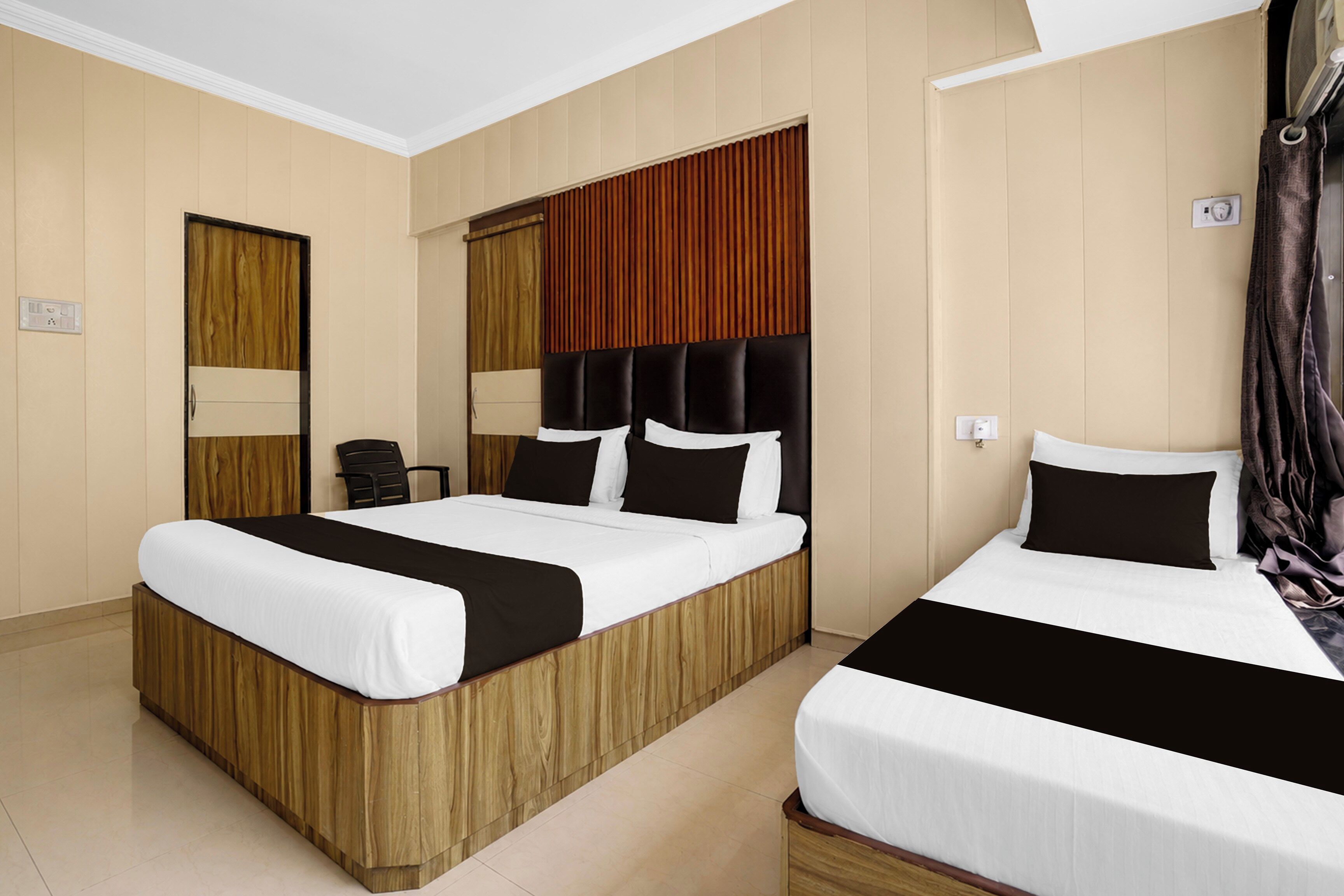 Habitación de hotel con dos camas, cabeceros de madera y un ventanal con cortinas.