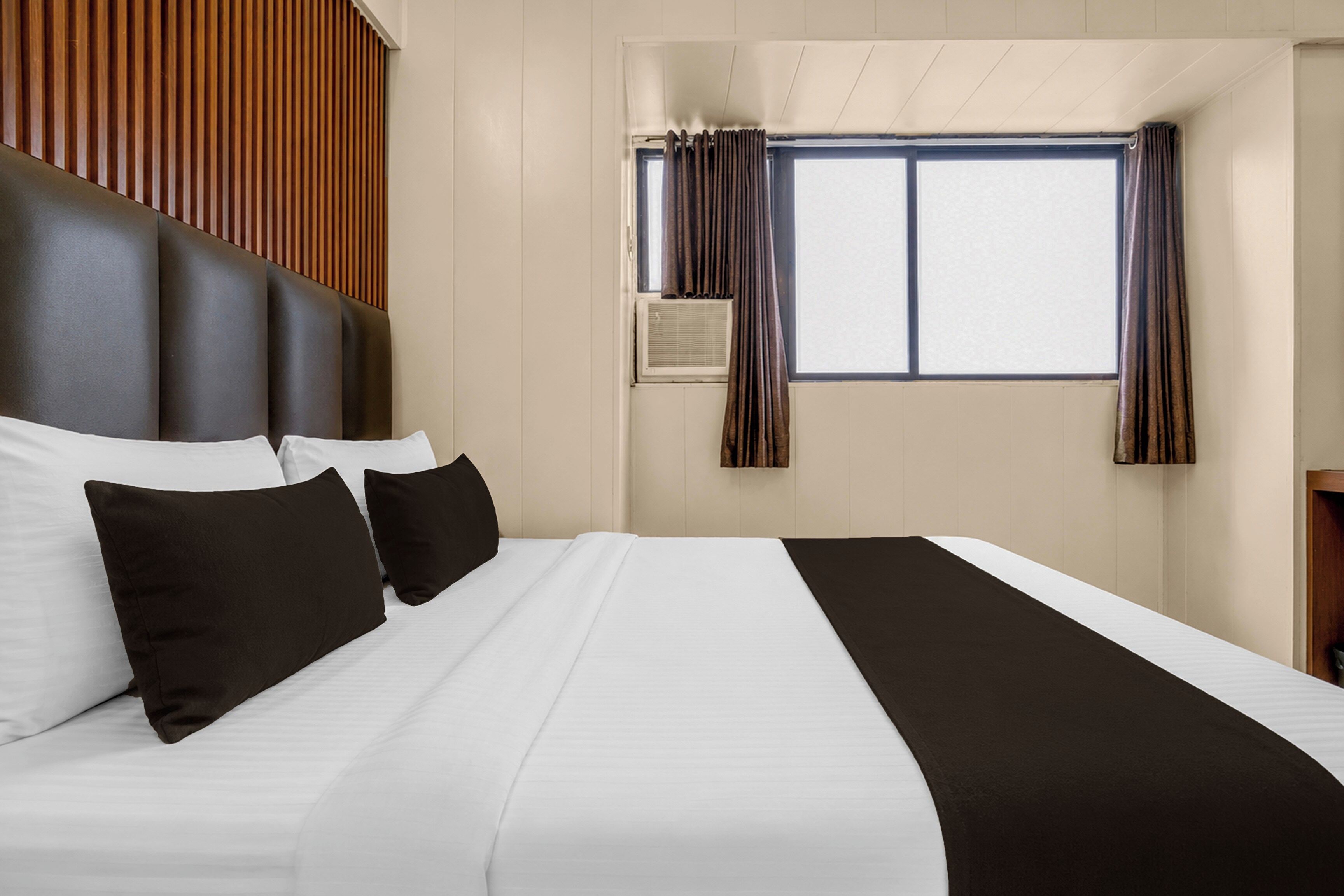 Una habitación de hotel con una cama grande, un cabecero, una ventana con cortinas y una pared de paneles de madera.