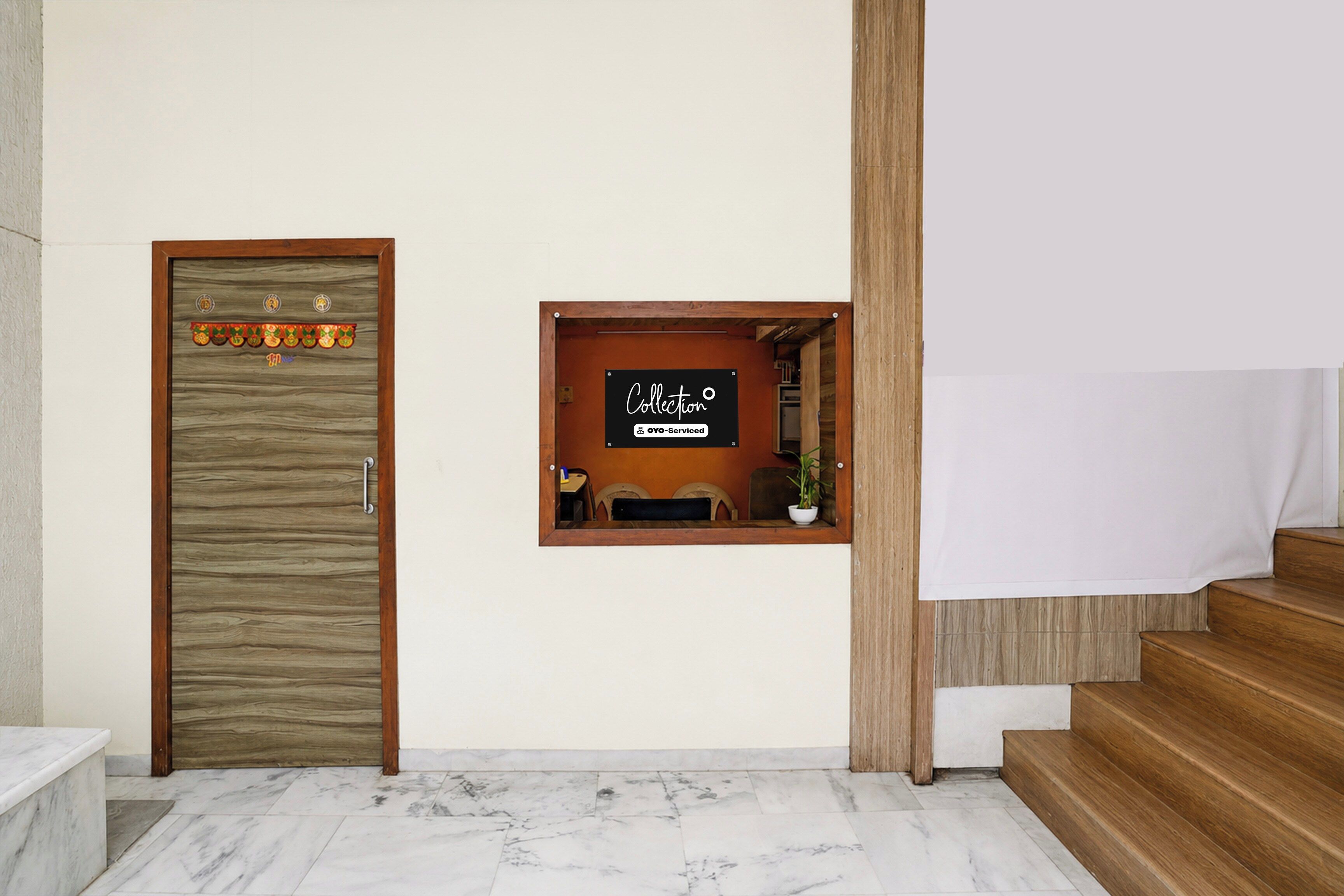 Un área de recepción con una puerta de madera, una ventana pequeña con un letrero y una escalera.