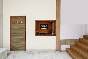 Un área de recepción con una puerta de madera, una ventana pequeña con un letrero y una escalera.