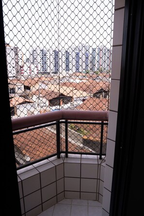 Ein Eckbalkon mit Metallgeländer, Fliesenboden und Blick auf Gebäude im Hintergrund.