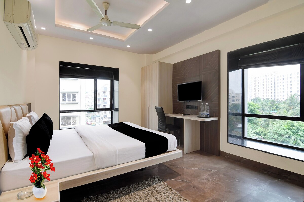A modern hotel room with a bed, a desk, a TV, and large windows.